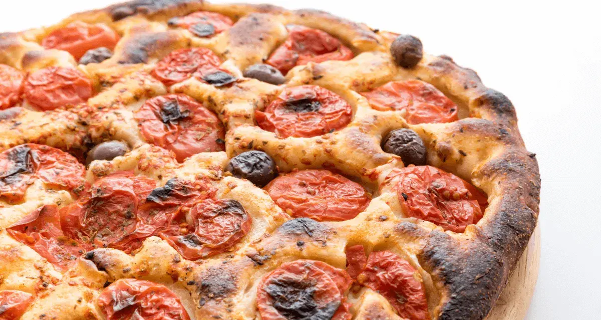 Focaccia barese dorata e fragrante, con pomodorini succosi e olive nere, pronta per essere gustata.
