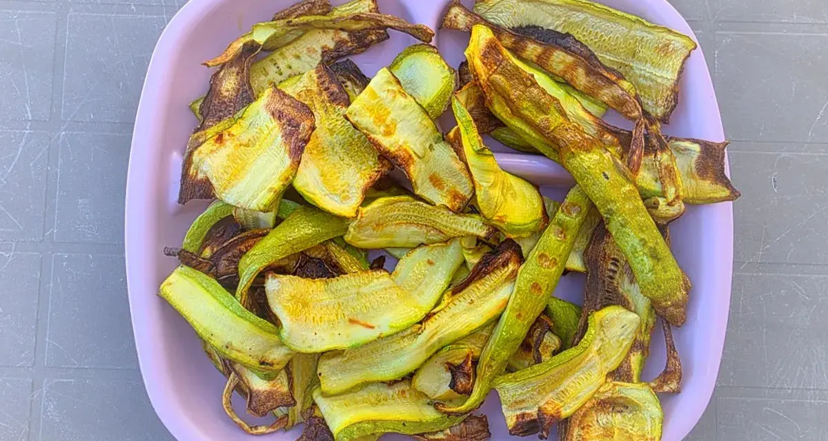 Piatto rosa pieno di zucchine grigliate, tagliate a listarelle e leggermente abbrustolite, pronte per essere gustate.