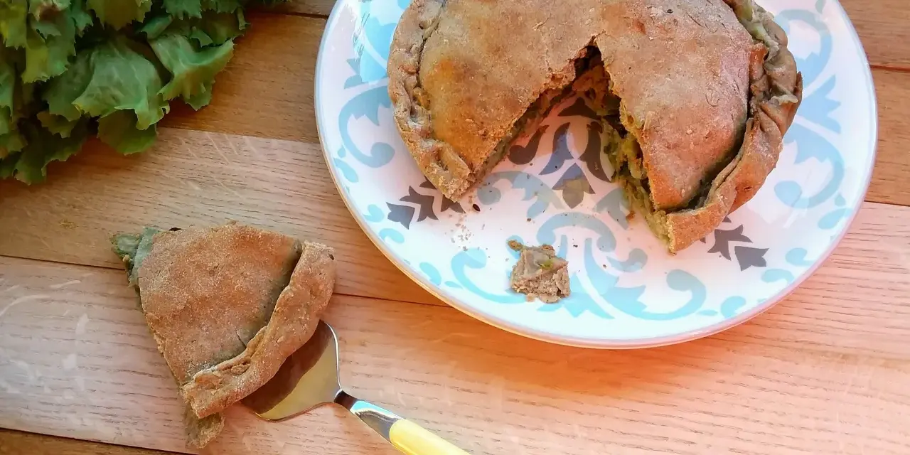 Torta salata con scarola, acciughe e mozzarella, appena sfornata, con una fetta servita su un piatto decorato.