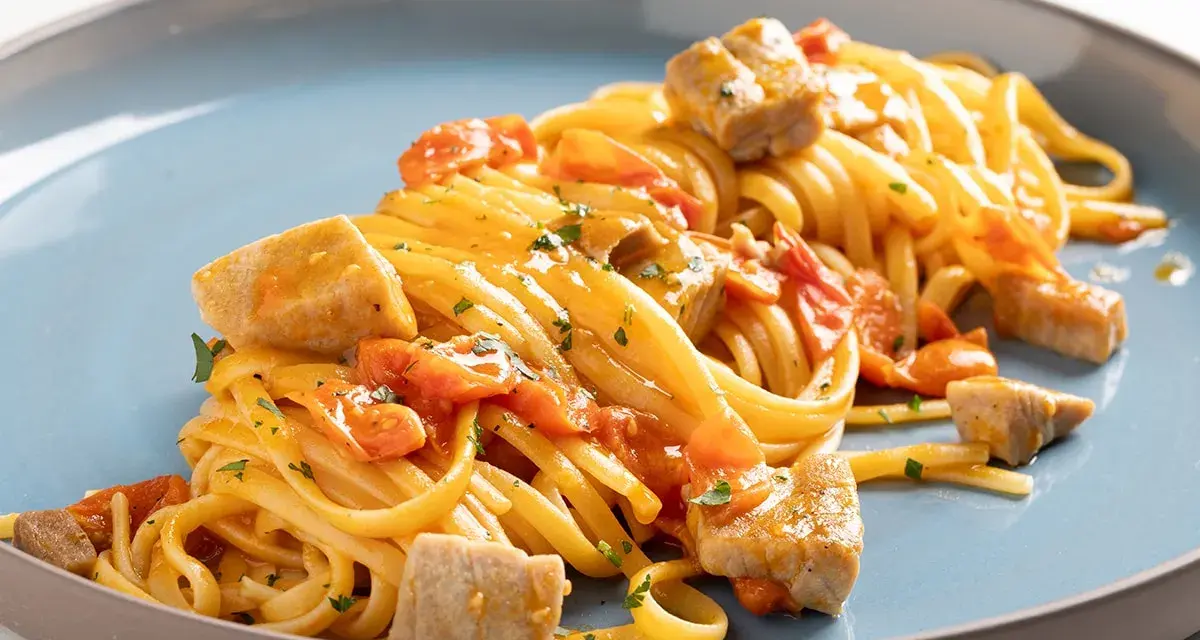 Un piatto invitante di pasta con tonno fresco, pomodorini e prezzemolo, condito con una salsa dorata.
