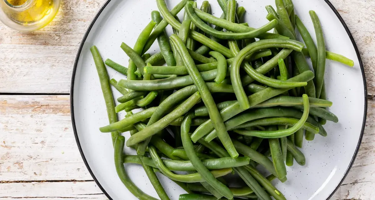 Un piatto di fagiolini lessi, freschi e verdi, pronti per essere gustati. Accanto, un piccolo recipiente con olio d'oliva.
