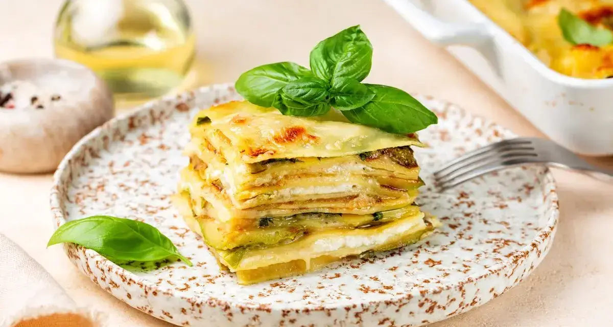 Una fetta di parmigiana di zucchine, stratificata e dorata, guarnita con basilico fresco.