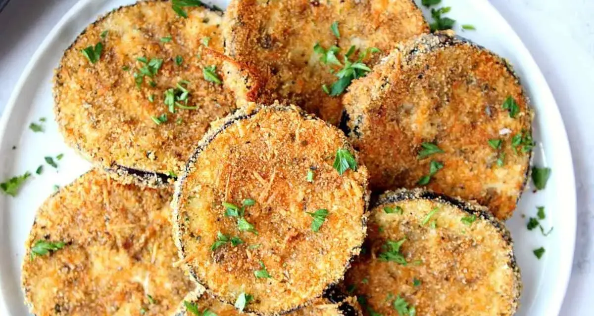 Fette dorate di melanzane impanate al forno, guarnite con prezzemolo fresco. Un antipasto croccante e saporito.
