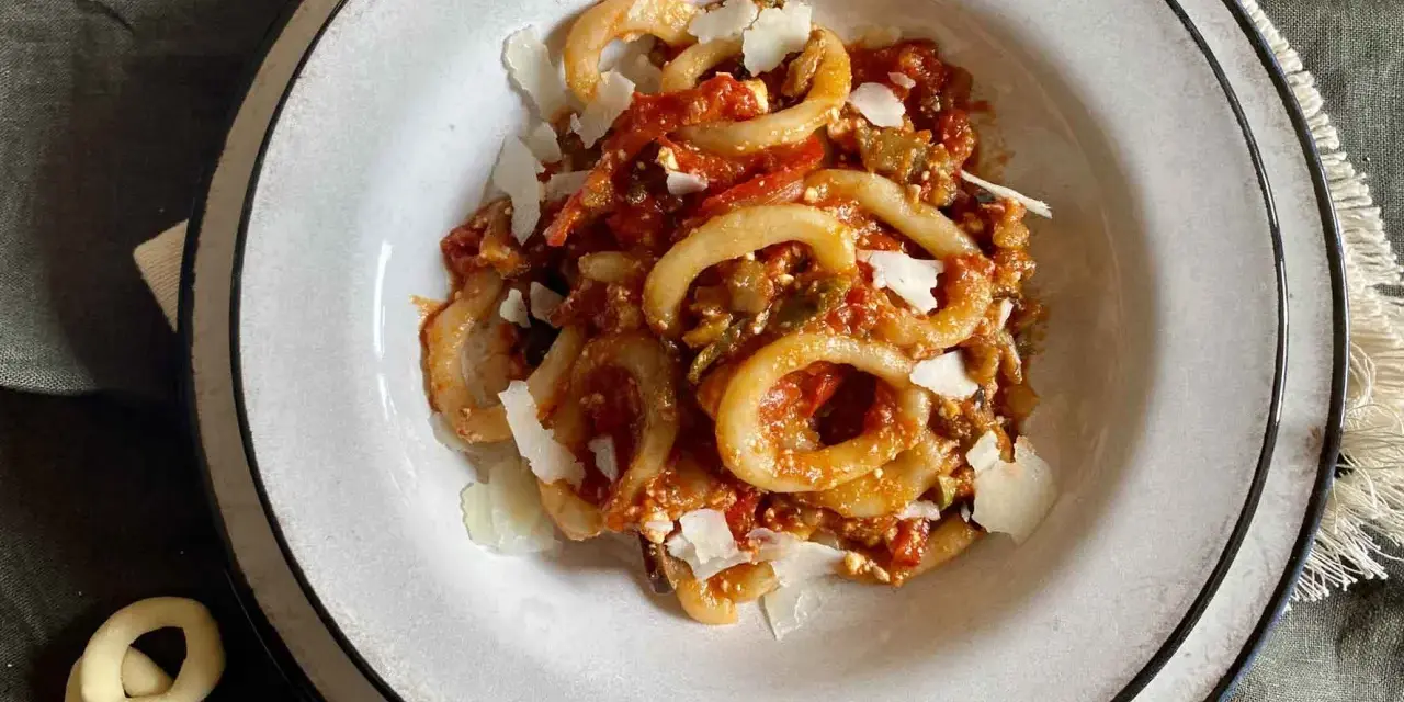 Un piatto di anellini alla pecorara, pasta a forma di anello condita con sugo di pomodoro, verdure e scaglie di formaggio.