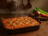 Anelletti alla siciliana fumanti in teglia, con ingredienti freschi sullo sfondo.