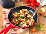Melanzane in padella con pomodoro e mozzarella, guarnite con olive e basilico. Un antipasto invitante e saporito.