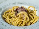 Un piatto di bigoli in salsa, con pasta spessa e condimento a base di acciughe e cipolla, guarnito con prezzemolo tritato.
