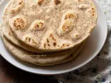 Piatto di piadine senza strutto, dorate e leggermente maculate, impilate su un piatto bianco.