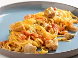 Un piatto invitante di pasta con tonno fresco, pomodorini e prezzemolo, condito con una salsa dorata.