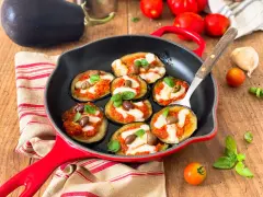 Melanzane in padella con pomodoro e mozzarella, guarnite con olive e basilico. Un antipasto invitante e saporito.
