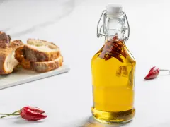 Olio al peperoncino in bottiglia, con pane rustico e peperoncini rossi. Un tocco piccante per ogni piatto.