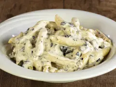 Penne cremose con pezzetti scuri, un piatto invitante di pasta alla cenere, servito in una ciotola bianca su un tavolo di legno rustico.