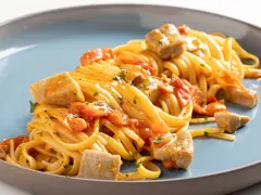 Un piatto invitante di pasta con tonno fresco, pomodorini e prezzemolo, condito con una salsa dorata.