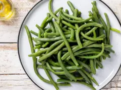 Un piatto di fagiolini lessi, freschi e verdi, pronti per essere gustati. Accanto, un piccolo recipiente con olio d'oliva.