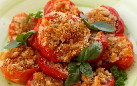 Pomodori al forno ripieni di pangrattato e erbe aromatiche, guarniti con basilico fresco.