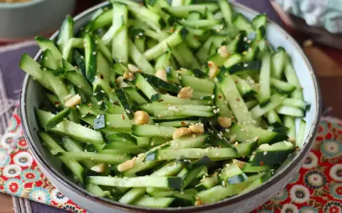 Una ciotola piena di fresca insalata di cetrioli tagliati a julienne, condita con semi di sesamo e arachidi croccanti.