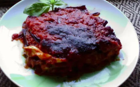 Una porzione di parmigiana di melanzane napoletana, ricca e saporita, guarnita con basilico fresco.