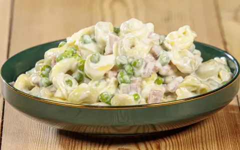 Un piatto invitante di tortellini panna e prosciutto, con piselli verdi, conditi con una cremosa salsa bianca.