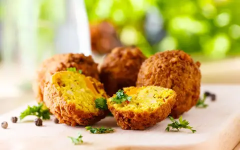 Polpette di ceci dorate e croccanti, cotte in friggitrice ad aria, guarnite con prezzemolo fresco su tagliere di legno.