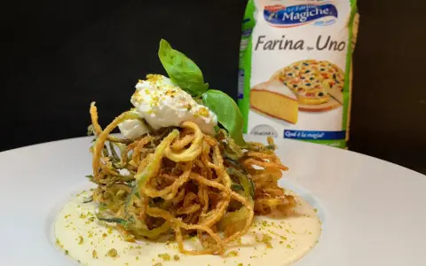 Deliziosi spaghetti di zucchine fritte croccanti, serviti su una crema vellutata e guarniti con ricotta fresca e basilico.