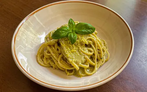 Spaghetti conditi con un cremoso pesto di limone, guarniti con basilico fresco. Una deliziosa ricetta per un primo piatto estivo.