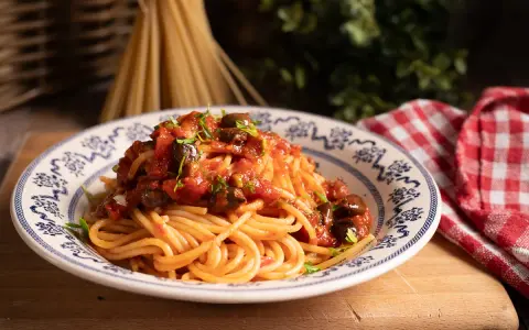 Piatto di spaghetti alla puttanesca, conditi con pomodoro, olive e capperi, guarniti con prezzemolo fresco.