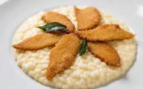 Un cremoso risotto al pesce persico, guarnito con filetti dorati e foglie di salvia croccante, un piatto che invita alla degustazione.