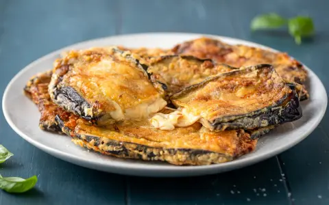 Melanzane contorno dorate e filanti, un piatto invitante con formaggio fuso e basilico fresco.