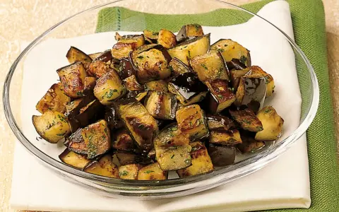 Melanzane a funghetto ricetta della nonna: cubetti dorati e saporiti, conditi con erbe aromatiche, in una ciotola di vetro.