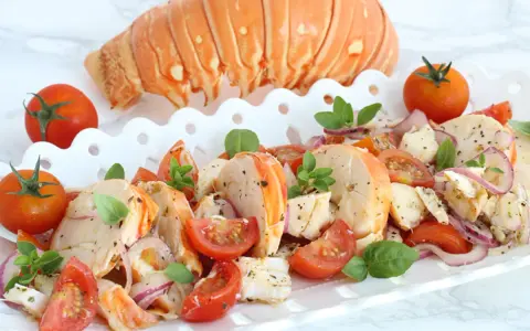 Aragosta alla catalana, un piatto fresco con aragosta, pomodorini, cipolla rossa e basilico, servito su un vassoio bianco.