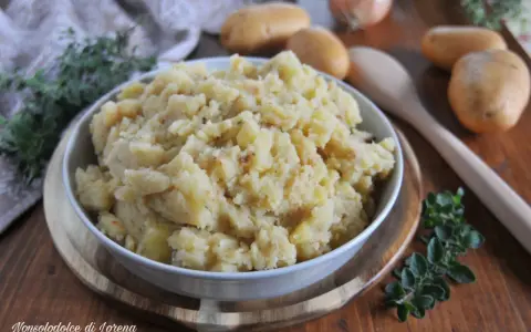 Un saporito piatto di patate in tecia, cotte con erbe aromatiche e spezie, servite in una ciotola su un tagliere di legno.
