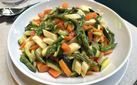Un piatto invitante di verdure in padella: asparagi, carote e zucchine tagliate a pezzetti, condite con un filo d'olio.