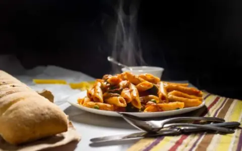 Piatto fumante di penne alla vodka, con pane croccante e posate pronte per gustare questo classico italiano.