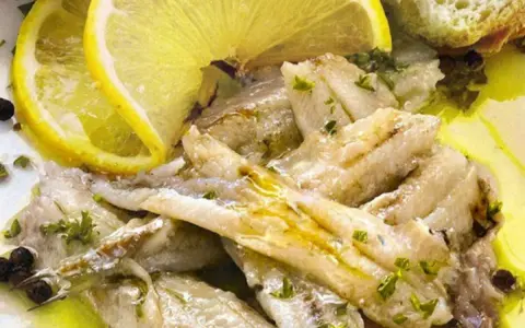 Alici in padella, succulente e dorate, condite con limone fresco, prezzemolo e pepe nero. Un piatto semplice e gustoso.