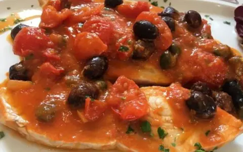 Delizioso pesce spada al forno con pomodorini, olive nere e capperi, un piatto saporito e colorato.