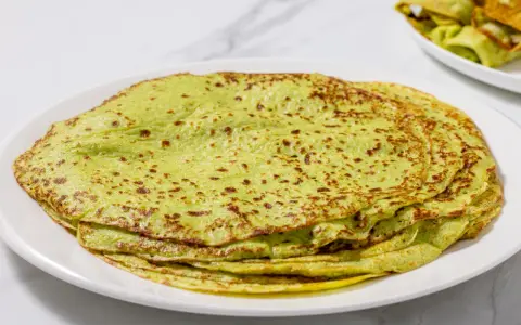 Piatto di crepes di zucchine verdi, sottili e leggermente dorate, impilate su un piatto bianco.