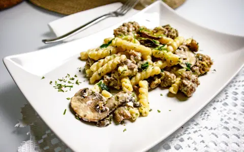 Un piatto di pasta salsiccia e funghi, condito con prezzemolo fresco, servito su un piatto bianco.