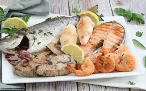 Un piatto invitante di grigliata di pesce: orata intera, tranci di salmone, gamberi, calamari e tonno, guarnito con limone e prezzemolo.