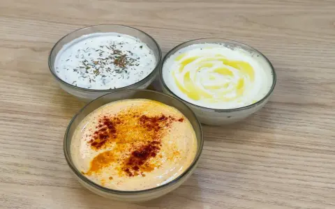 Tre ciotole di salsa con yogurt greco: una con erbe, una con olio d'oliva e una con paprika.