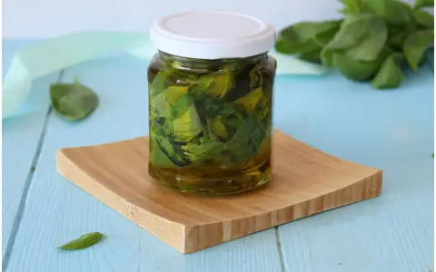 Un vasetto di basilico sott'olio, con foglie fresche sullo sfondo, pronto per insaporire i tuoi piatti.