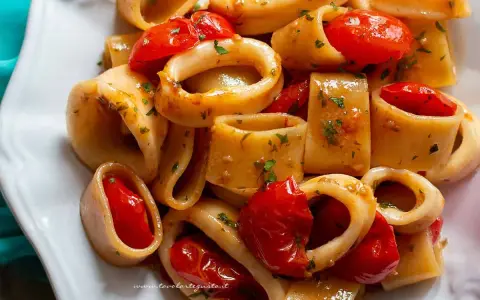 Un invitante sugo di pesce con anelli di calamaro e pomodorini, guarnito con prezzemolo fresco.