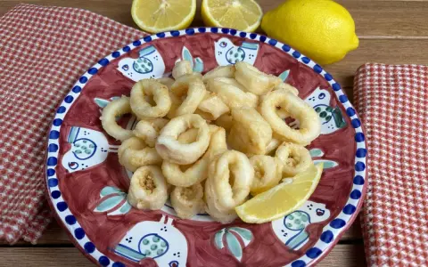 Un piatto di **calamari fritti** dorati, guarnito con spicchi di limone fresco, su un piatto decorato con uccelli stilizzati.