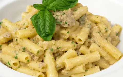 Un piatto di pasta con melanzane in bianco cremosa, condita con erbe aromatiche e guarnita con una foglia di basilico fresco.