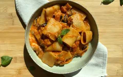 Un piatto di pasta alla siciliana con rigatoni, melanzane e una salsa cremosa al pomodoro, guarnito con basilico fresco.
