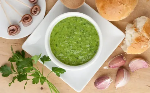 Un invitante bagnetto verde piemontese, accompagnato da acciughe arrotolate, pane fresco e spicchi d'aglio.