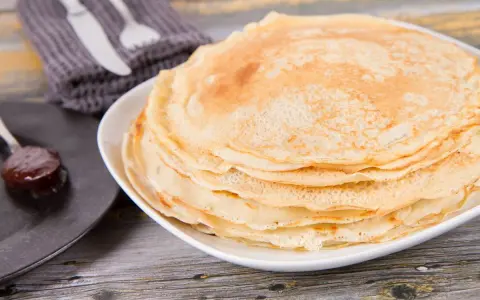 Pila di crepes senza uova, dorate e soffici, pronte per essere farcite. Accanto, un cucchiaino di marmellata.