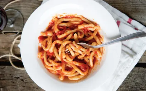 Piatto di pasta fresca condita con un saporito sugo all'aglione, servito su un piatto bianco con una forchetta.