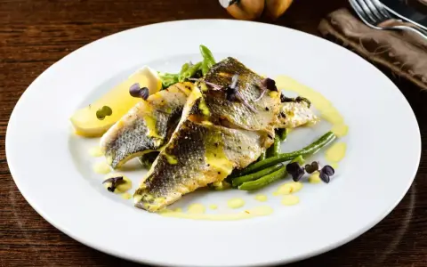 Deliziosi secondi di pesce con fagiolini croccanti, limone e una salsa gialla cremosa, guarniti con erbe viola.