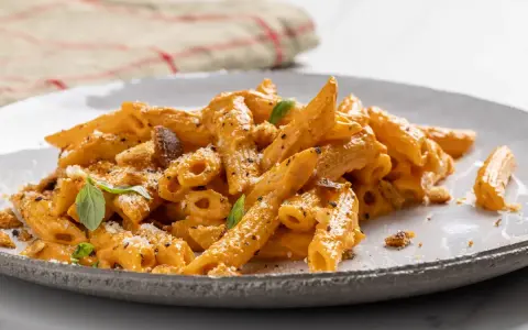 Penne con una ricca crema di peperoni, guarnite con basilico fresco e crostini croccanti. Un piatto invitante e saporito.