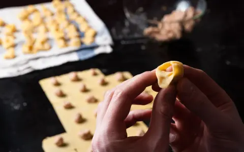 Mani che creano tortellini fatti in casa, con la pasta fresca e il ripieno pronto.